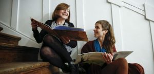 Foto de Leonor Beuter y Maria Rosa Lojo posando en una escalera sosteniendo ejemplares del libro Las Siniguales.